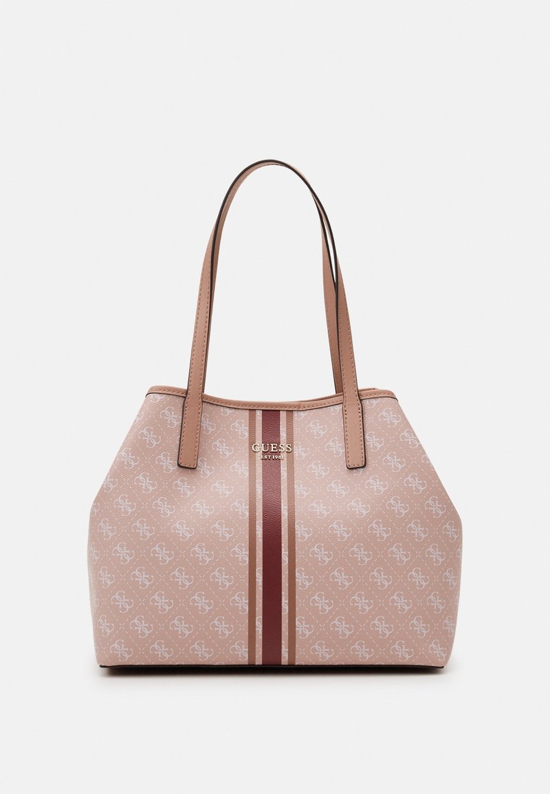 Vaaleanpunainen kantokassi, jossa on logokuosi, kaksi ruskeaa kahvaa ja keskeinen raita vaihtelevissa ruskeissa sävyissä. Rakenne on teksturoitua materiaalia, jossa on sileitä yksityiskohtia.