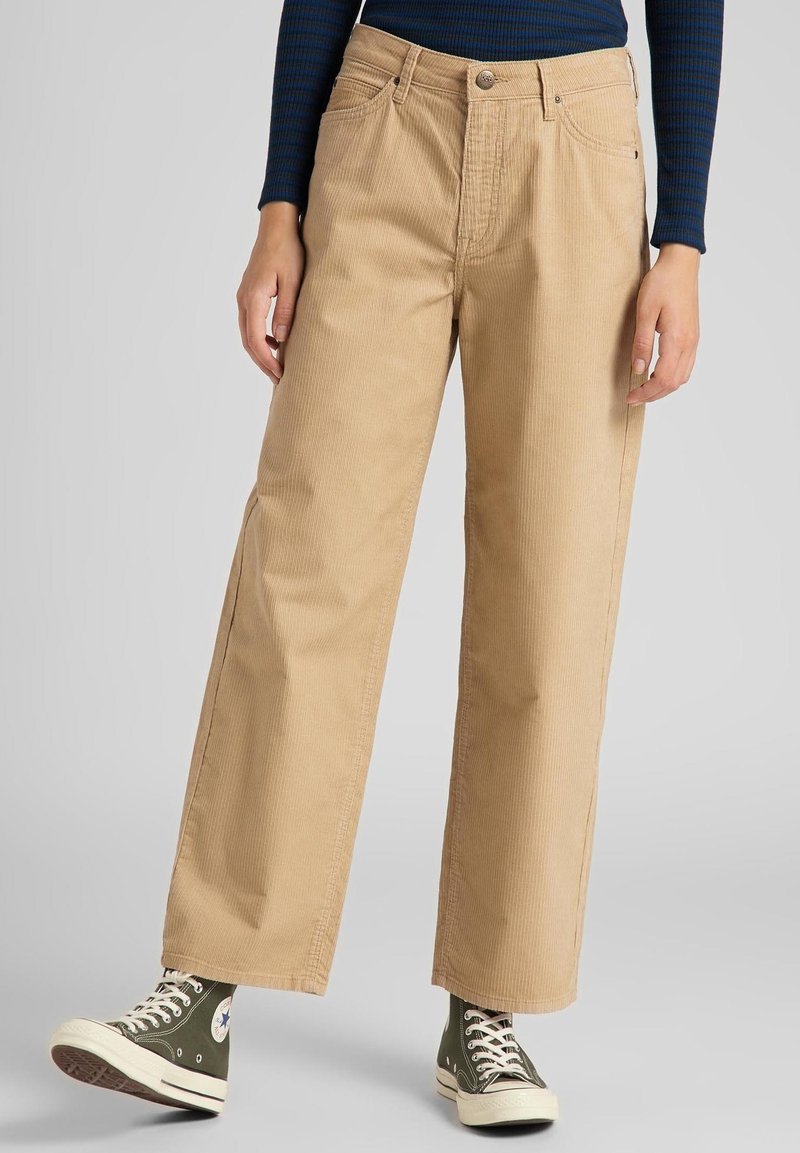 Beige cordflätade vida byxor med hög midja, framfickor och knappstängning, kombinerat med gröna kanvas sneakers.