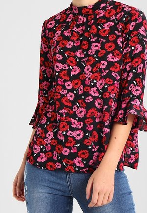 Czarna bluzka z czerwono-różowym kwiatowym wzorem, rękawy do połowy przedramienia zakończone falbanami, zestawiona z niebieskimi, przetartymi jeansami.