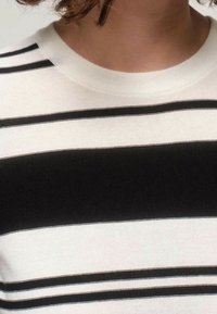 Černo-bílý pruhovaný pletený svetr s kulatým výstřihem. Pruhy se liší tloušťkou a vytvářejí texturovaný vzhled.