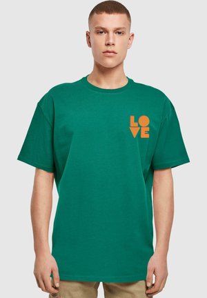 Grøn bomulds T-shirt med løs pasform, med orange "LOVE" grafik på venstre bryst. Korte ærmer og rund halsudskæring.