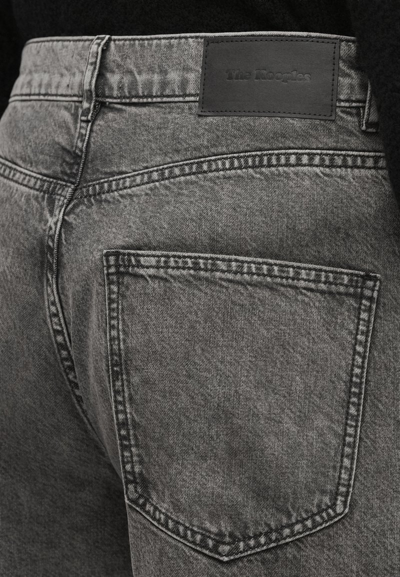 Close-up of back pocket and waistband of faded black denim jeans with stitched label reading "The Kooples."