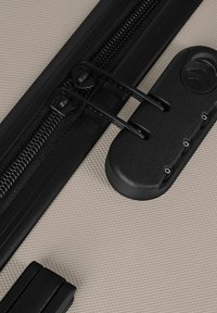 Primer plano de una maleta beige con textura, con dos tiradores de cremallera negros asegurados en una cerradura de combinación de tres dígitos incorporada.