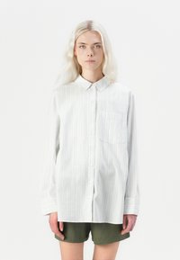 Camicia con bottoni in leggero tessuto di cotone, caratterizzata da righe verticali blu e bianche, colletto, maniche lunghe e taschino frontale.