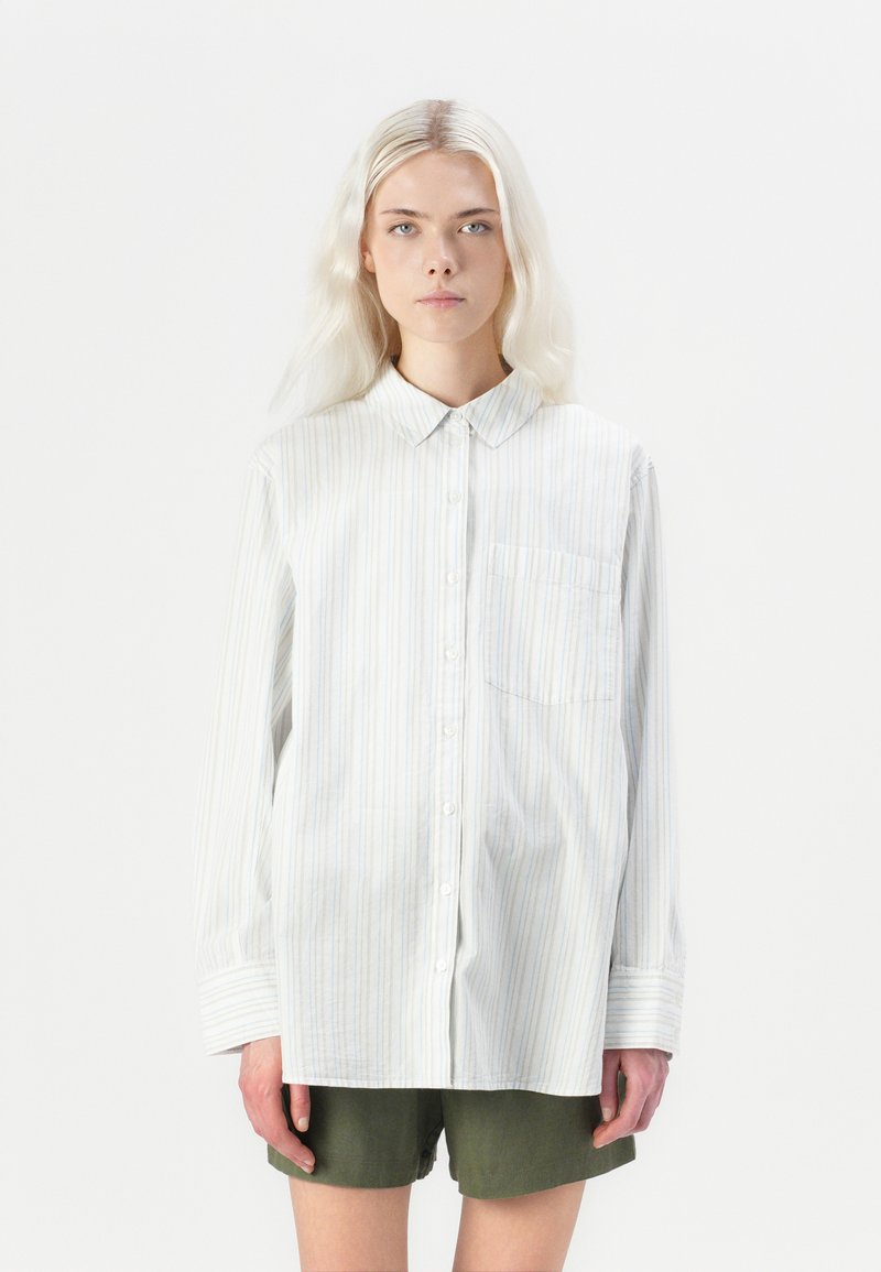 Camicia con bottoni in leggero tessuto di cotone, caratterizzata da righe verticali blu e bianche, colletto, maniche lunghe e taschino frontale.