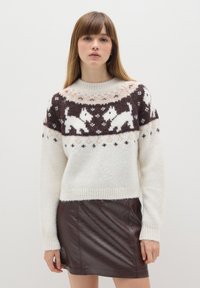 Strickpullover in Creme, Braun und Rosa mit einem grafischen Design von weißen Hunden. Weiche Textur, gerippte Bündchen und runder Halsausschnitt. Dunkelbrauner Lederrock.
