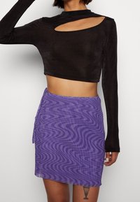 Svart långärmad crop top med utskärning och en lila minikjol med ett vågigt mönster. Båda plaggen har en slät yta.