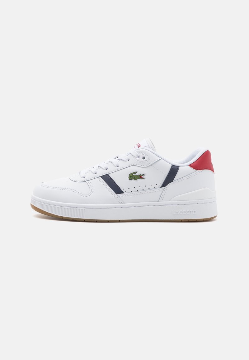 Baskets blanches Lacoste avec rayures bleu marine, logo crocodile vert, languette rouge au talon et semelle en gomme sur fond neutre.