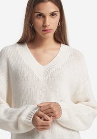 Vit, stickad tröja med v-hals, som har ribbade muddarna och ett strukturerat mönster. Löst sittande med en mjuk känsla.