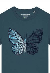 T-shirt teal avec un graphique d'un papillon bleu aux motifs d'ailes géométriques, tracé en noir, centré sur le devant.