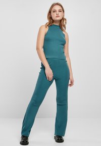 Teal ribbet strik to-delt sæt med en ærmeløs mock neck top og tætsiddende flared bukser, med en glat tekstur og minimalistisk design.