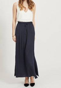 Marinblå maxikjol med avslappnad passform, elastisk midja och sidofickor. Matchad med en vit ärmlös topp och svarta klackar.