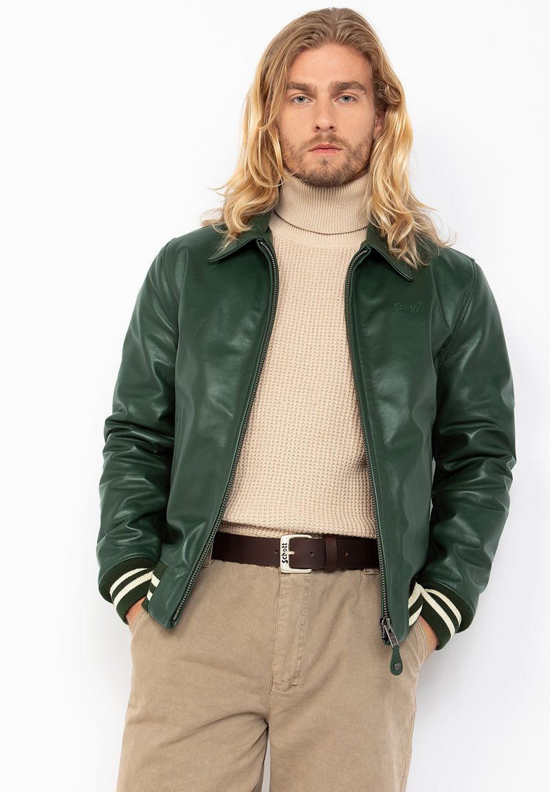 Groene leren bomberjack met witte en groene gestreepte ribgebreide manchetten, ritssluiting en een gladde afwerking. Draagt over een beige gebreide coltrui.