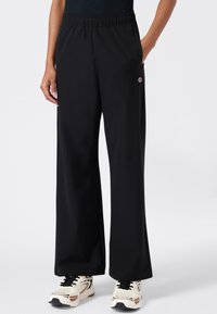 Zwarte broek met wijde pijpen, gemaakt van zachte, gladde stof met een elastische tailleband en zijzakken. Kenmerkt zich door een klein logo op de linkerheup.
