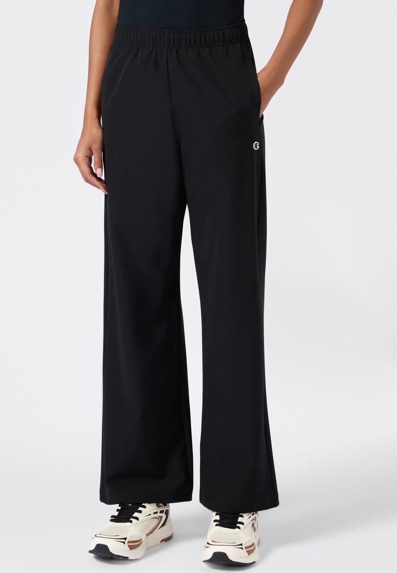 Zwarte broek met wijde pijpen, gemaakt van zachte, gladde stof met een elastische tailleband en zijzakken. Kenmerkt zich door een klein logo op de linkerheup.