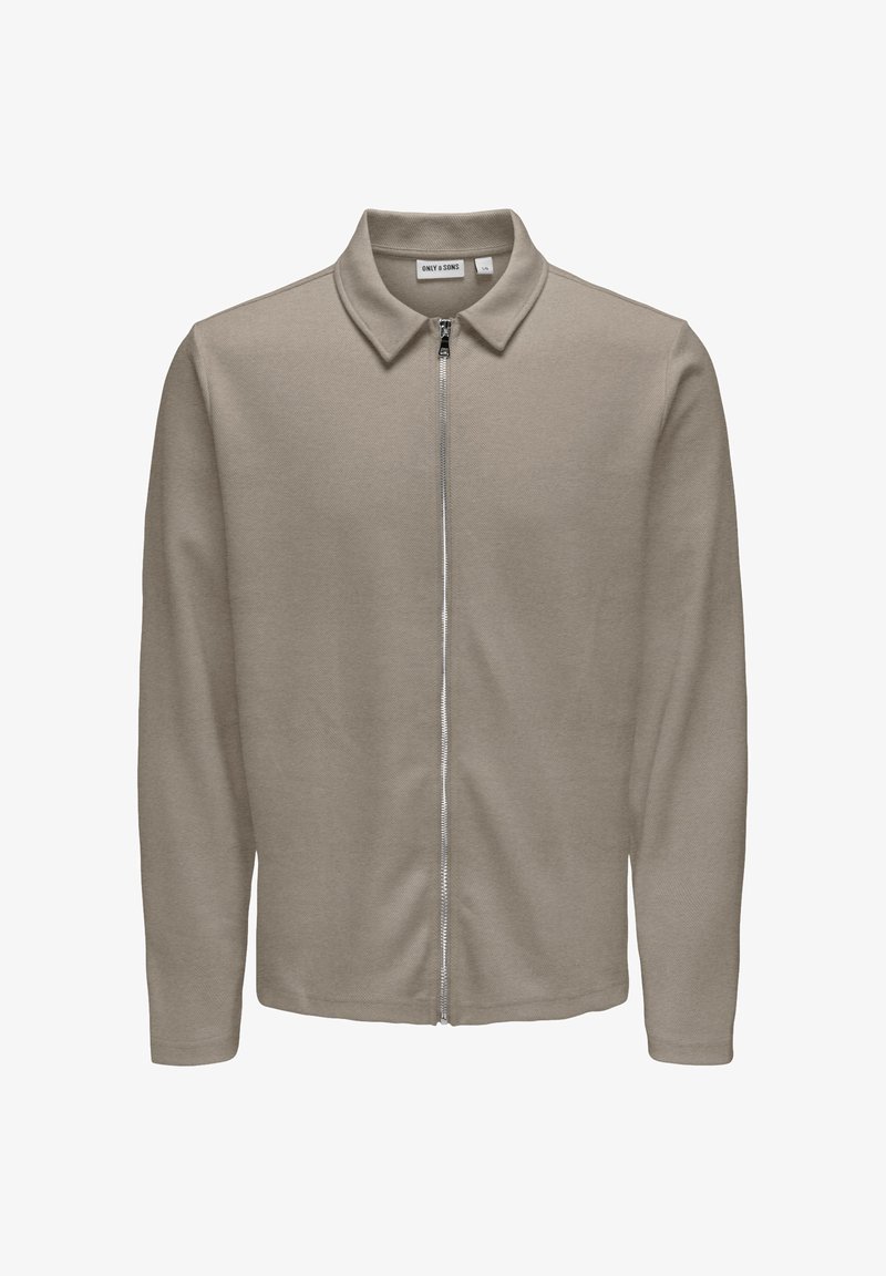 Veste à manches longues brun clair avec fermeture éclair et col, en tissu texturé, dotée d'une fermeture éclair centrale argentée et d'une étiquette de marque à l'intérieur du col.