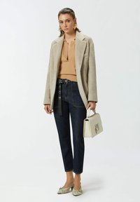 Blazer beige in misto lana sopra un maglione marrone a coste, abbinato a jeans scuri a vita alta e una borsa color crema; accentuato con tacchi a punta.