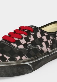Μαύρο και ροζ καρό αθλητικό παπούτσι Vans με φθαρμένη σόλα, κόκκινα κορδόνια και ορατό λογότυπο Vans στο πλάι.