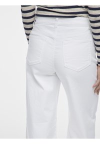 Jeans de mezclilla blanca con una cintura de altura media, bolsillos traseros y un ajuste ligeramente holgado. El material es suave con una textura lisa.