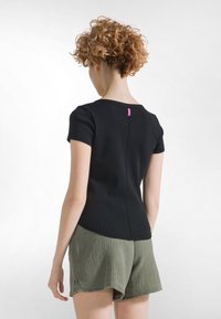 Černý top s krátkými rukávy a kulatým výstřihem, zdobený vertikálním švem a růžovou štítkem na zadní straně. Doplněný olivově zelenými texturovanými šortkami.