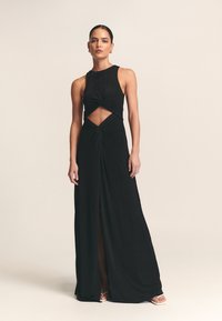 Musta maksimekko, valmistettu pehmeästä kankaasta, jossa on halter-kaulus, kiertodetalji, vyötäröllä leikattu alue ja eteen sijoitettu halkio visuaalisen kiinnostavuuden lisäämiseksi.