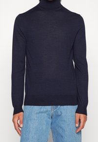 Námořnický rolák s dlouhými rukávy, vyrobený z jemně pleteného materiálu, s přiléhavým střihem a žebrovanými manžetami a lemem. Zobrazuje ležérní vzhled.