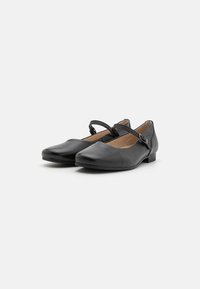Schwarze Leder-Ballerinas mit runder Spitze, einem einzelnen Knöchelriemen und niedrigem, gestapeltem Absatz. Glatte Textur und minimalistisches Design.