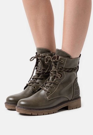 Bottes en cuir vert olive avec un design à lacets, panneau arrière texturé et semelle en caoutchouc marron ; elles présentent des coutures renforcées et des œillets en métal.