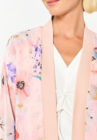 Blommig kimono i mjuk rosa genomskinlig väv med metalliska inslag. Har en kontrasterande ljusrosa ribbad krage och en flödande silhuett.