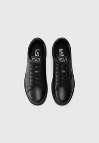 Adidași negri din piele cu o textură netedă, vârf rotund, șireturi și logo EA7 pe limbă. Pe lateral sunt prezente linii și detalii subtile.