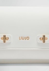 Hvid tekstureret læderhåndtaske med guldfarvet hardware, der har en tryklåsbindung og et præget "LIUJO" logo på fronten.