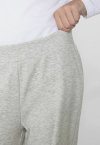 Světle šedé tepláky s jemnou texturou, elastickým pasem a bočními kapsami, které představují uvolněný střih a minimální designové detaily.