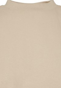 Close-up van een beige shirt met ronde hals gemaakt van geribbelde stof, met zicht op de kraag en het bovenste deel van de borst.