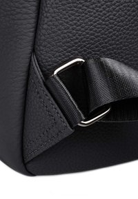 Angolo di una borsa di pelle nera con superficie testurizzata, cuciture a contrasto, un anello a D in metallo argentato e una tracolla in nylon nero.
