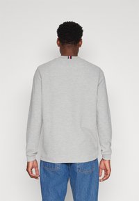 Harmaa pitkähihaine huppari, jossa on pyöreä kaula-aukko ja pieni punainen, valkoinen ja sininen raita korostus takana. Yhdistetty sinisiin farkkuihin.