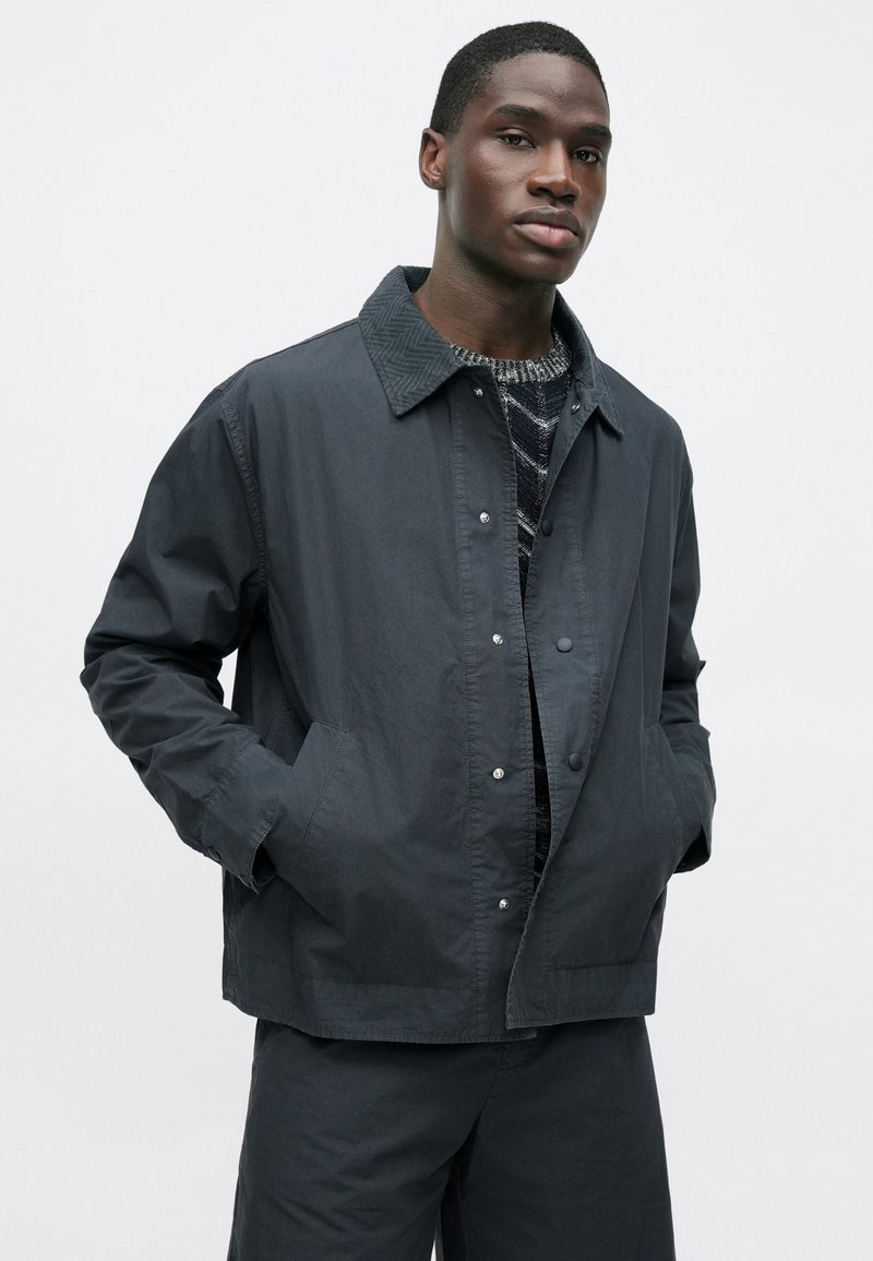 Dark gray button-up jacket with a textured collar, two front pockets, and a relaxed fit, made from lightweight material.