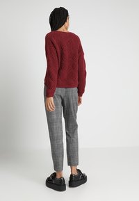 Bordowy sweter dziany ze wzorem fakturowanym, szare spodnie w kratę oraz błyszczące czarne buty na platformie widziane od tyłu.