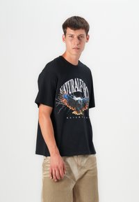 Sort bomuld t-shirt med korte ærmer, der har et farverigt ørn-grafik og teksten "NATURAL" over brystet. Slim-fit design.
