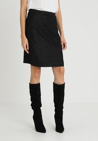 Zwarte glitterrok met een slim-fit ontwerp, tot de knie, met een gladde textuur en rechte zoom. Gecombineerd met zwarte suède laarzen tot de knie.