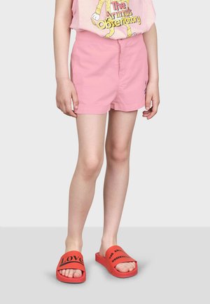 Shorts en coton rose avec une taille ajustée, associés à des sandales à glissière rouges portant le texte noir "LOVE" et un grand logo.
