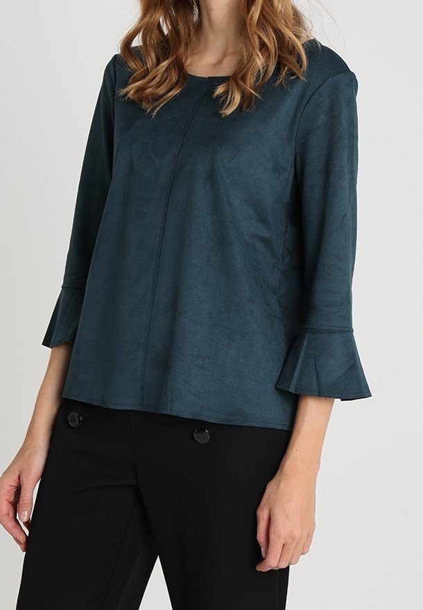 Top in finta suede color teal con maniche a campana a tre quarti, scollatura rotonda e una texture sottile, abbinato a pantaloni neri con bottoni.