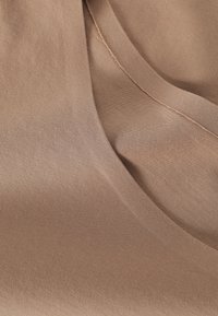 Lysebrunt stof med en glat overflade, der har en subtil glans og en buet kant, som viser et sømløst design og fine syningsdetaljer.