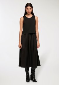 Czarny top bez rękawów o luźnym fasonie, zestawiony z długą czarną spódnicą. Gładka faktura materiału, dopełniające całość czarne botki do kostek.