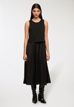 Top nero senza maniche con vestibilità ampia, abbinato a una lunga gonna nera. Tessuto morbido, stivali neri alla caviglia completano l'outfit.