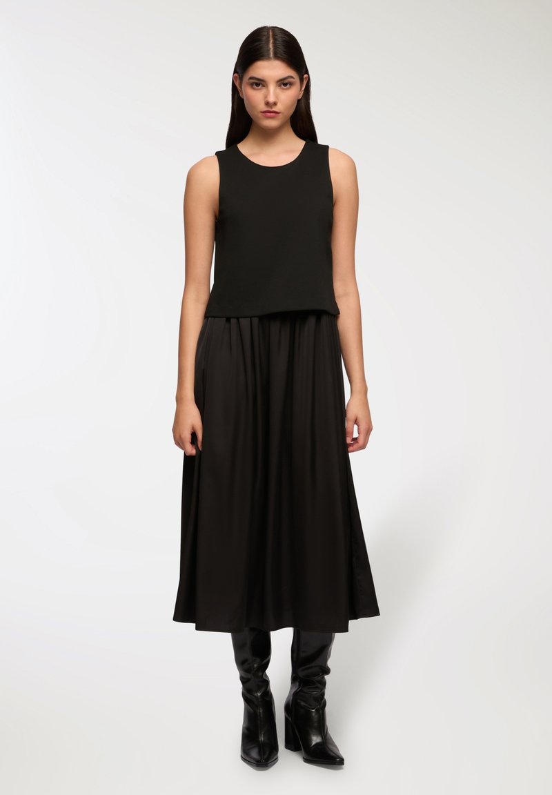 Czarny top bez rękawów o luźnym fasonie, zestawiony z długą czarną spódnicą. Gładka faktura materiału, dopełniające całość czarne botki do kostek.
