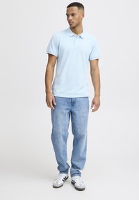 Svetlo modra polo majica s ovratnikom, v kombinaciji s svetlo modrimi jeans hlačami in belimi supergami z črnimi poudarki. Minimalističen dizajn in mehak material.