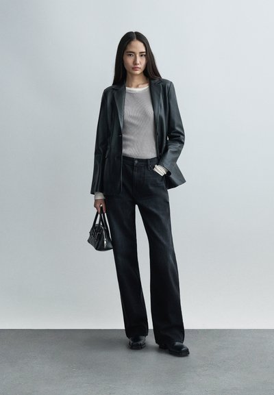 Μαύρο δερμάτινο σακάκι πάνω από γκρι ριμπ τοπ, συνδυασμένο με σκούρο τζιν φαρδιάς γραμμής. Μια μικρή τσάντα συμπληρώνει το ντύσιμο, με ουδέτερο φόντο.