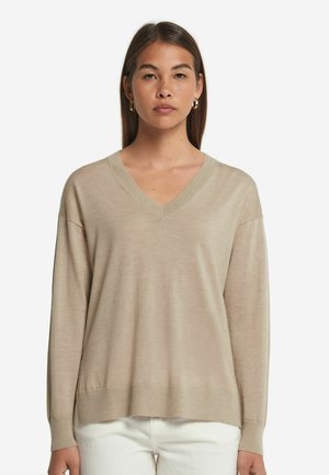 Beige v-hals sweater med lange, let løse ærmer. Ribbet halsudskæring og manchetter. Blød tekstur, båret med hvide bukser. Minimalistisk design.