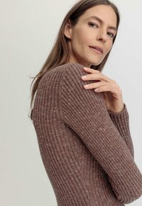 Rippenbraunes Sweatshirt mit langen Ärmeln, das ein strukturiertes Strickmuster und eine taillierte Silhouette aufweist, unterstrichen durch dezente Farbvariationen.
