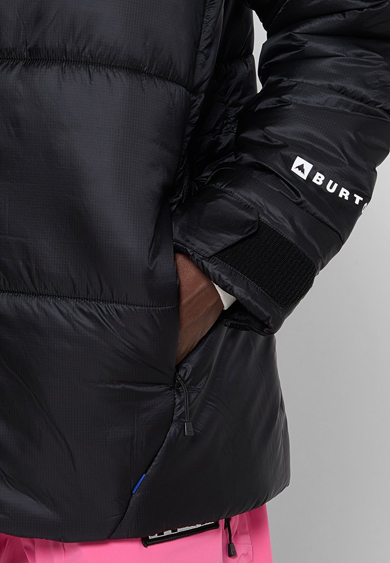 Schwarze Steppjacke mit einem gesteppten Design, ausgestattet mit Reißverschlusstaschen, elastischen Bündchen und einem auffälligen Logo auf dem Arm. Weiche, glänzende Textur.